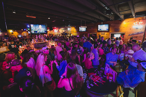 A crowded night at the bar with TVs overhead and the room washed in purple light