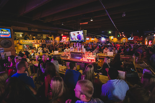 The center island bar stocked with backlit bottles, surrounded by a full evening crowd