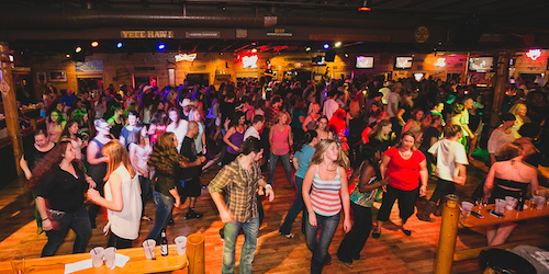 A packed dance floor of line dancers in step beneath the Yeee Haw! sign