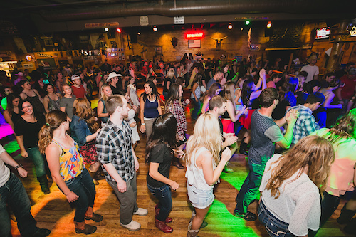 Dancers filling the wood dance floor beneath mounted steer horns and neon bar signs