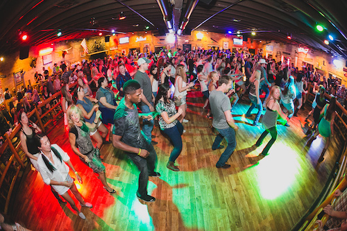 Line dancers moving together across the dance floor under green and red lights
