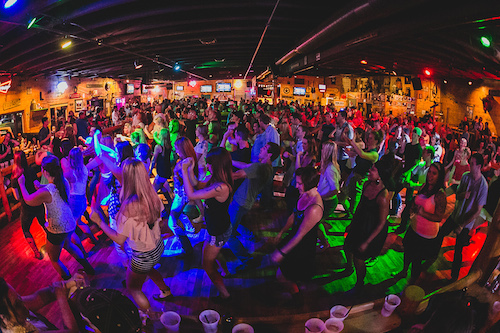 A full house of dancers crowding the floor, lit blue and green from the stage lights