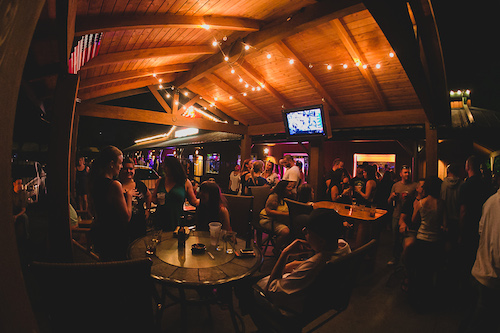 The timber-framed patio pavilion filled with guests beneath string lights and an American flag